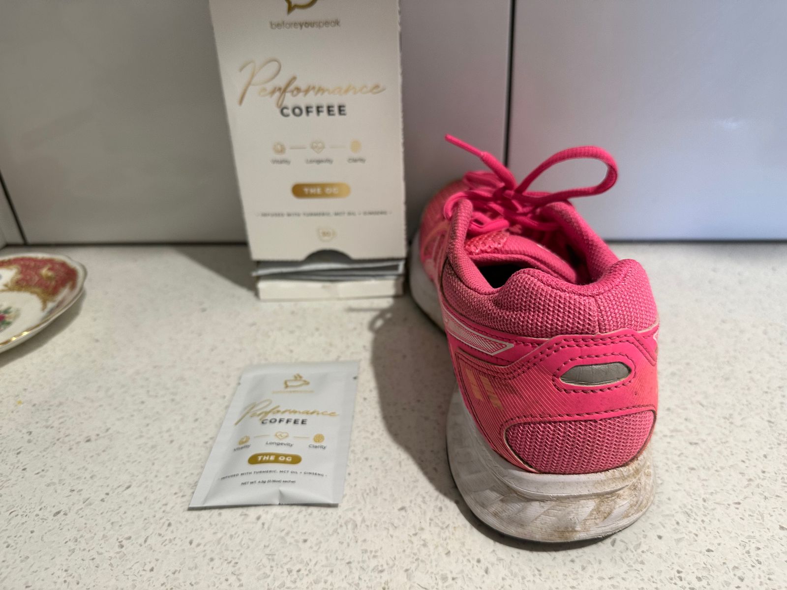 A Performance Coffee The OG box and sachet beside a pink running shoe
