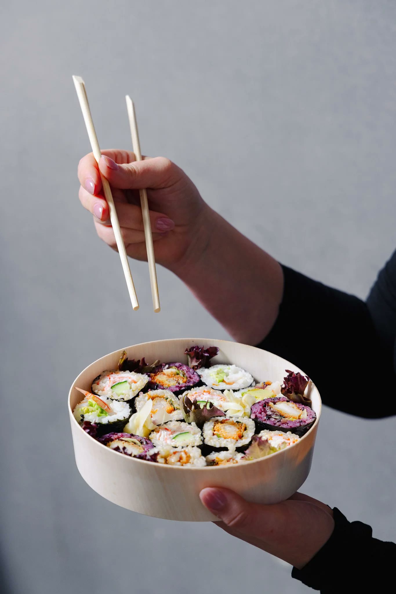 Chopsticks lifting a roll from a takeaway sushi box