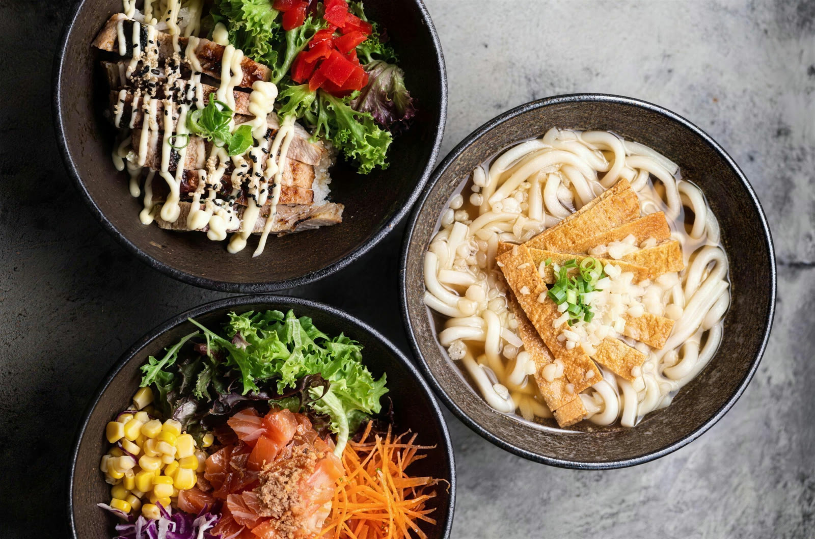 Udon noodles with tofu beside chicken and poke bowls