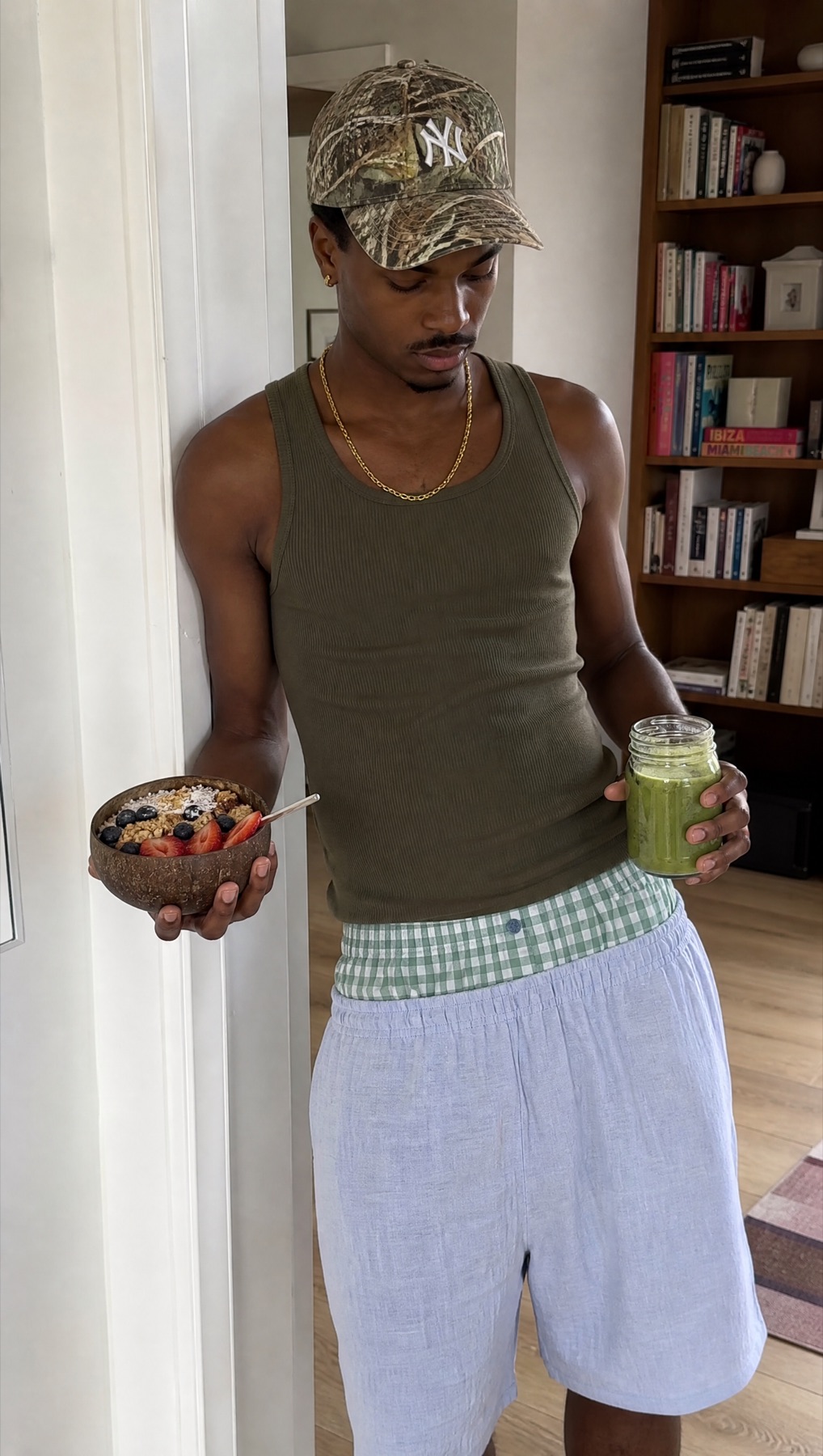 Model holding breakfast and a green smoothie with green check boxers visible above lounge shorts