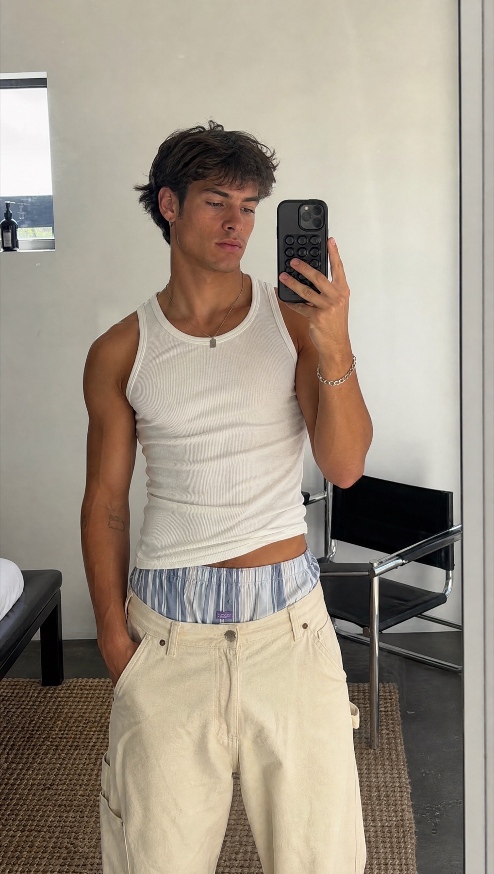 Model taking a mirror selfie with a blue striped boxer waistband above cream denim