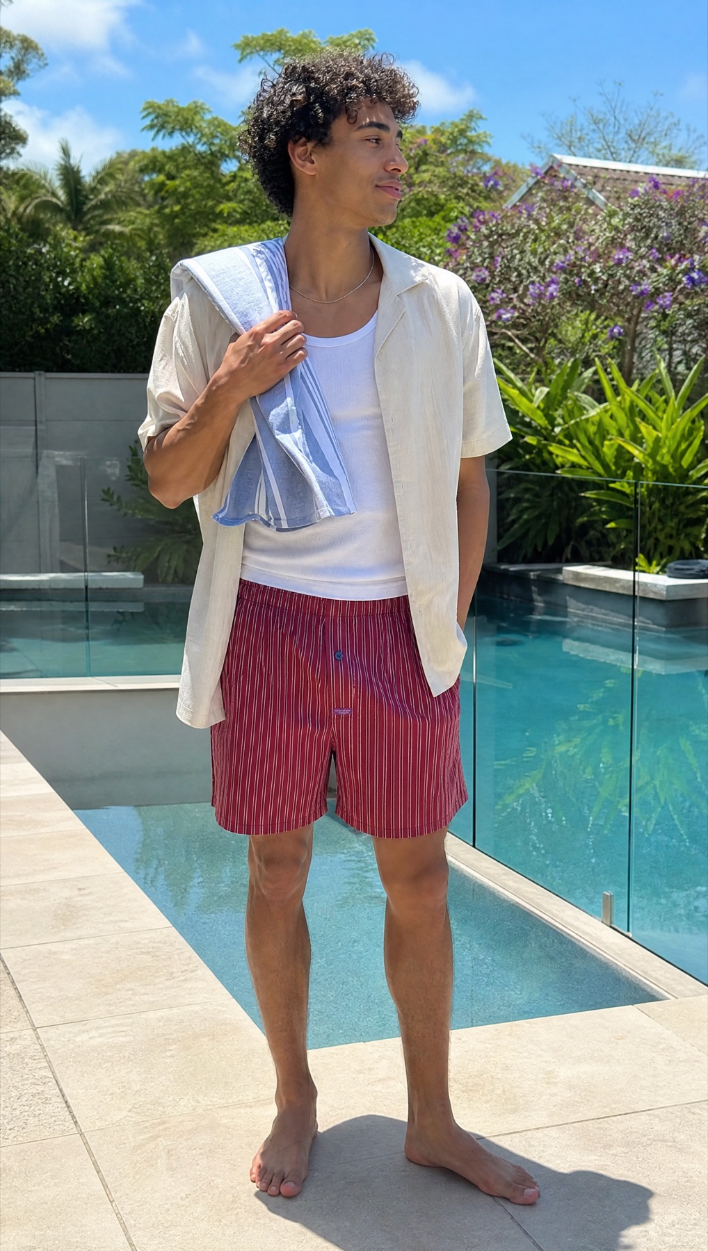 Model poolside wearing red striped Mitch Dowd boxer shorts with a tank and open shirt