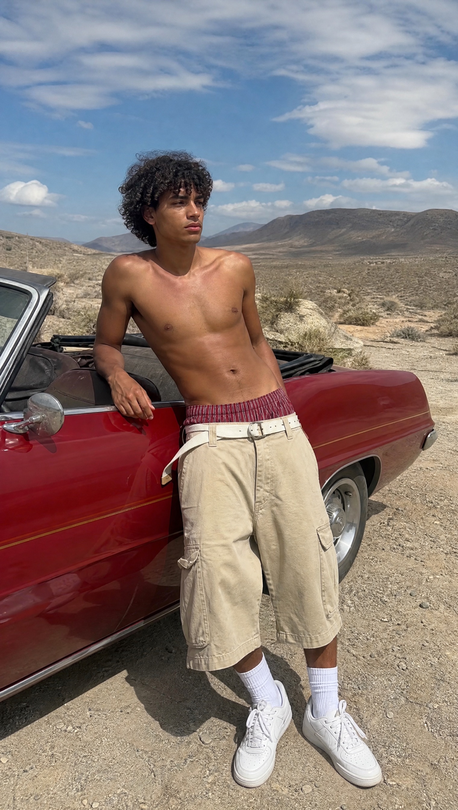 Model wearing a red striped boxer waistband beside a vintage red convertible in the desert