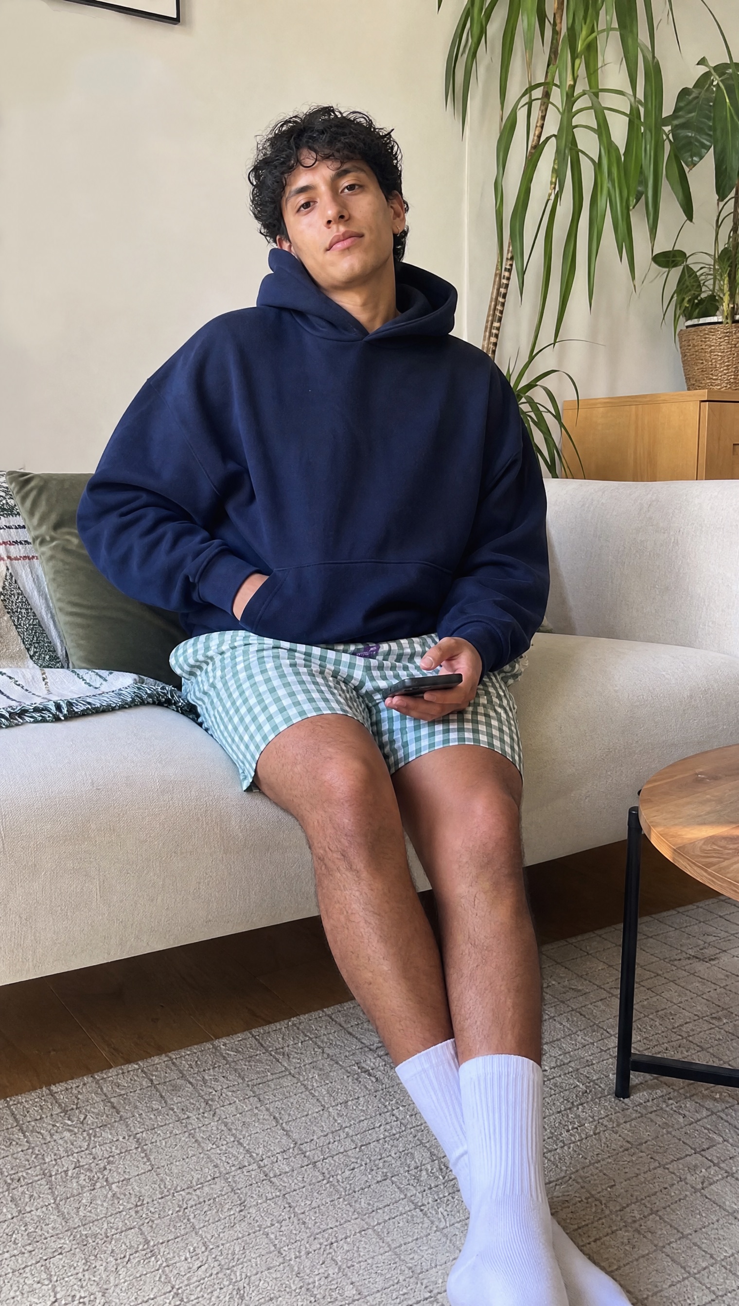 Model relaxing on a sofa in green check Mitch Dowd boxer shorts and a navy hoodie